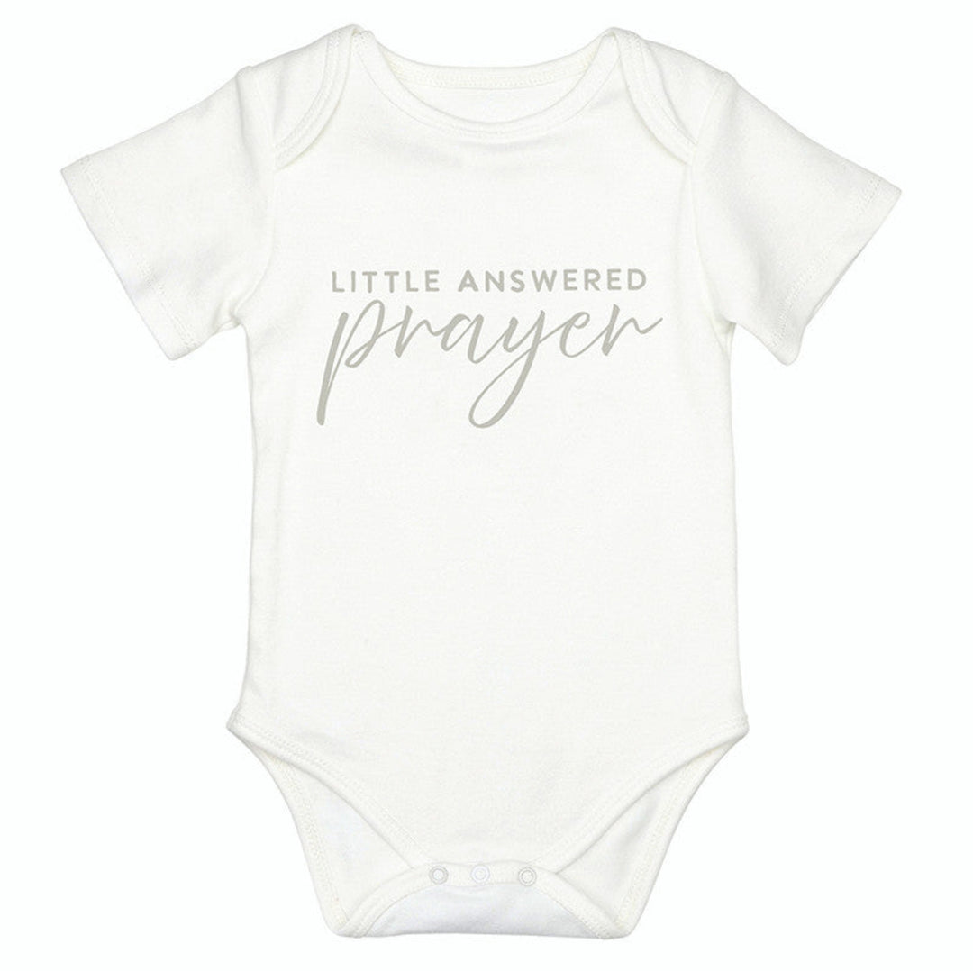 A white short-sleeve baby bodysuit with the text 'LITTLE ANSWERED prayer' printed in a light gray font on the chest, displayed against a solid white background.
