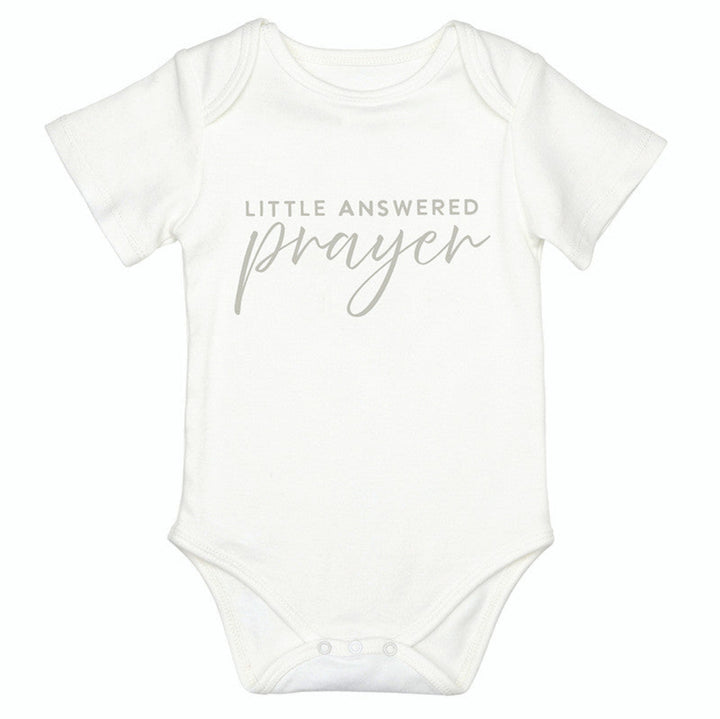 A white short-sleeve baby bodysuit with the text 'LITTLE ANSWERED prayer' printed in a light gray font on the chest, displayed against a solid white background.