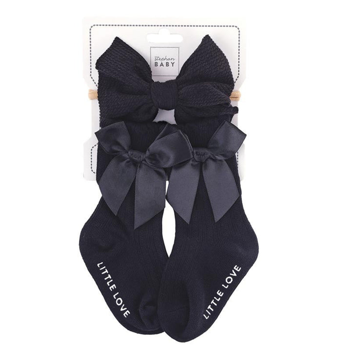 A pair of black baby socks with large matching bows on the toes, packaged on a white card labeled 'St. Lukes BABY'.