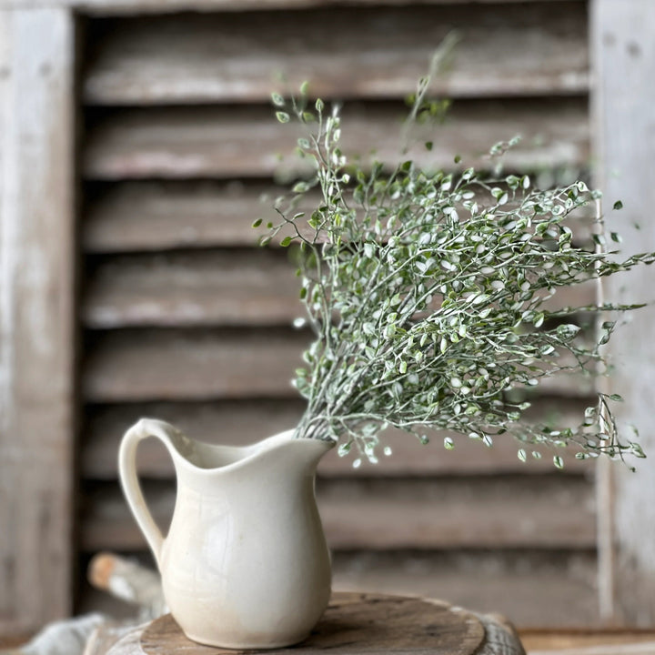 White pitcher with greenery on a wooden surface with rustic background