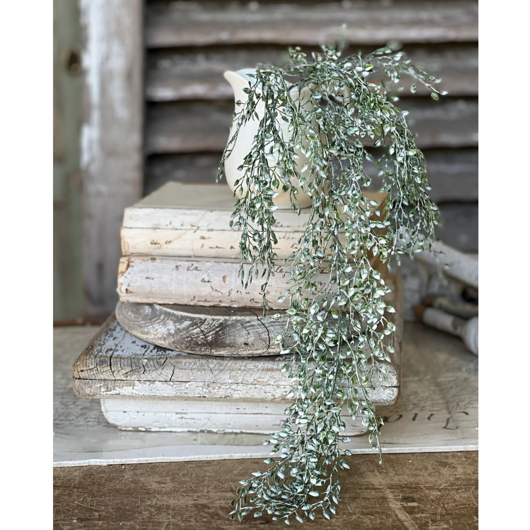 A faux green hanging foliage decoration placed on top of a stack of books.