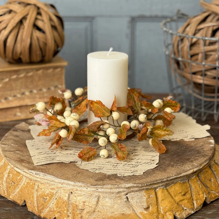 Decorative centerpiece with a candle, leaves, and berries on a wooden base.