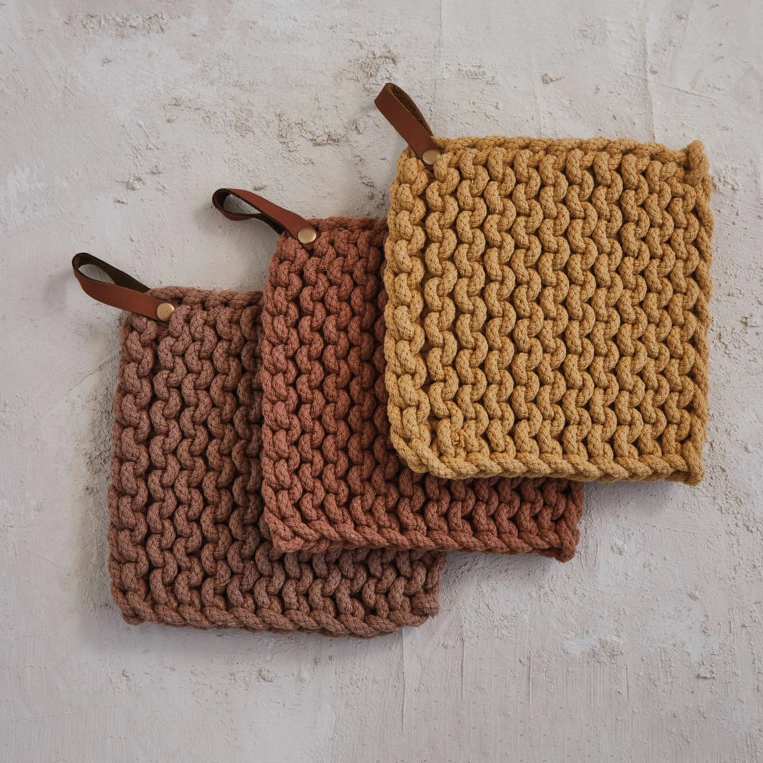 Set of three knitted pot holders with leather straps on a textured surface