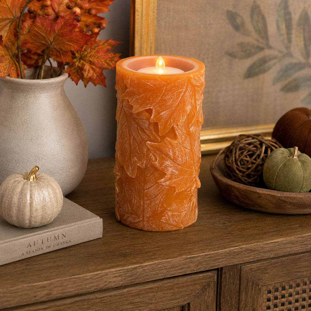 Decorative candle with leaf pattern on a wooden surface with pumpkins and leaves.