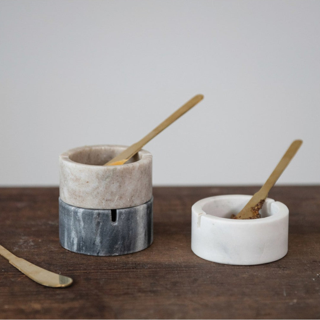 Two small ceramic containers with wooden spoons on a wooden surface.