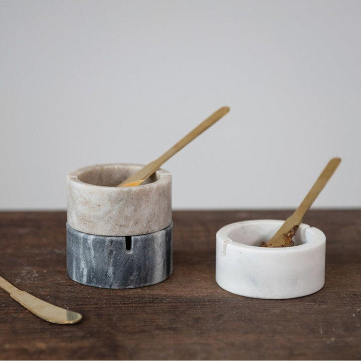 Two small ceramic containers with wooden spoons on a wooden surface.