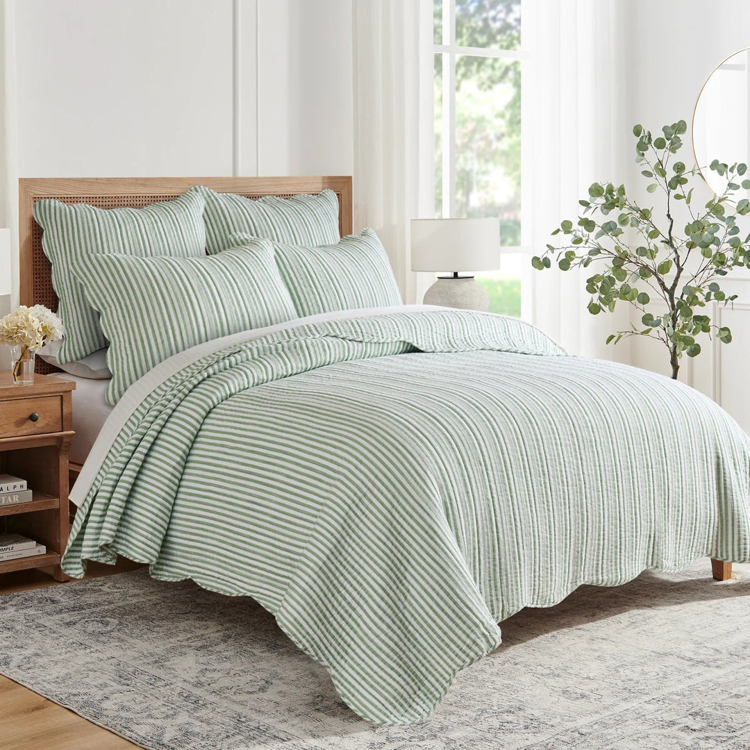Green striped bedding set on a bed in a bright bedroom with a plant and lamp.