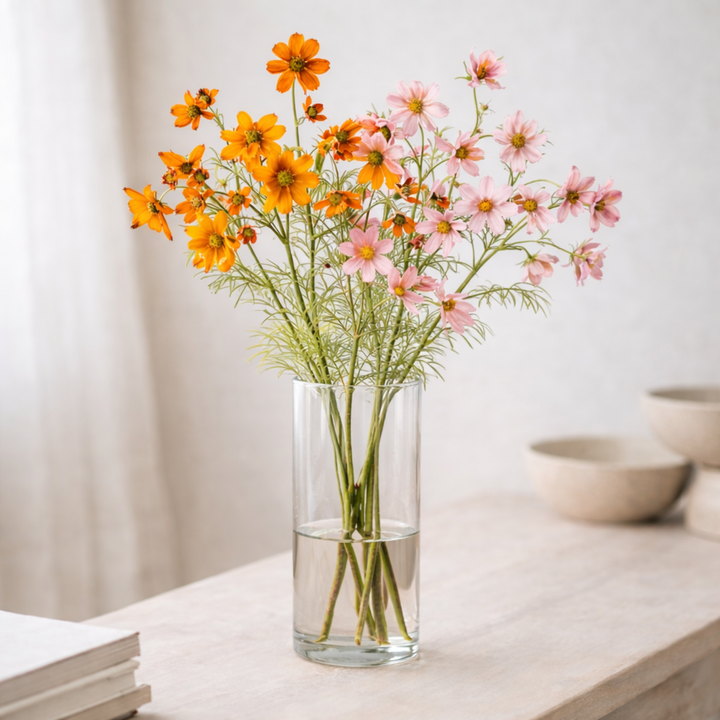 Clear glass vase with orange and pink flowers on a light surface