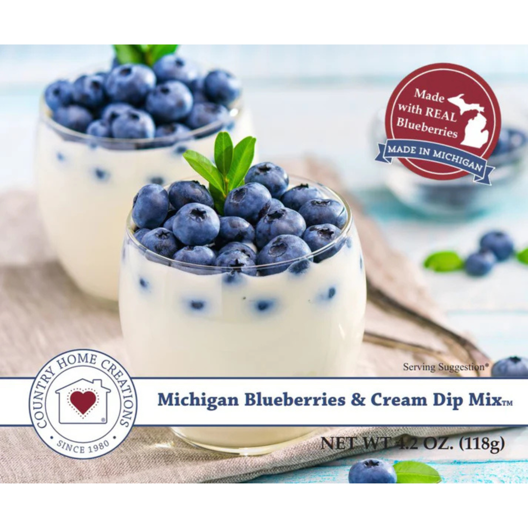 Two glass cups filled with creamy blueberry dip topped with fresh blueberries and mint leaves, with a 'Michigan Blueberries & Cream Dip Mix' label and a 'Made with Real Blueberries Made in Michigan' badge on a light blue background.