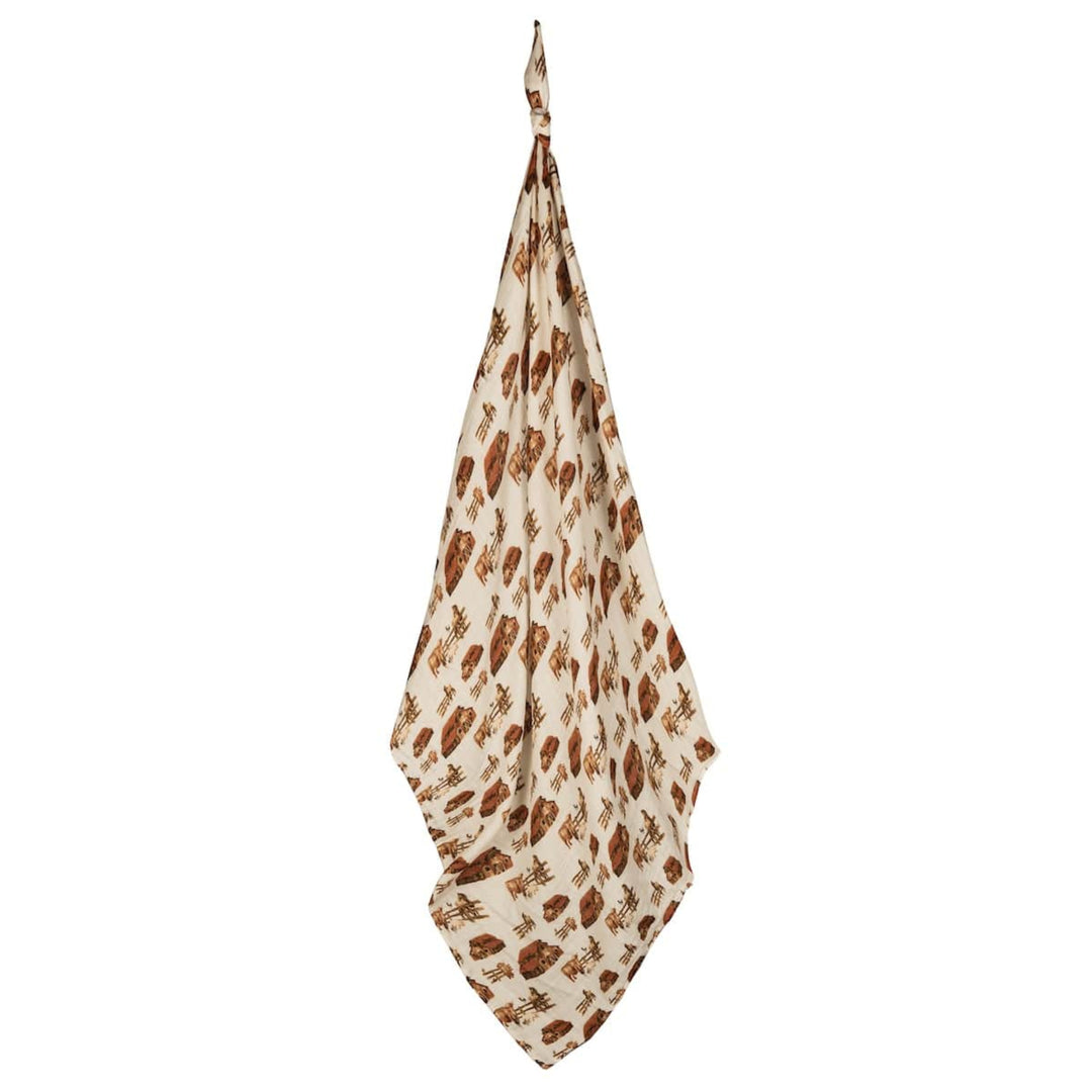 A beige and brown organic cotton Muslin Swaddle Blanket with a leaf print, hanging by one corner.
