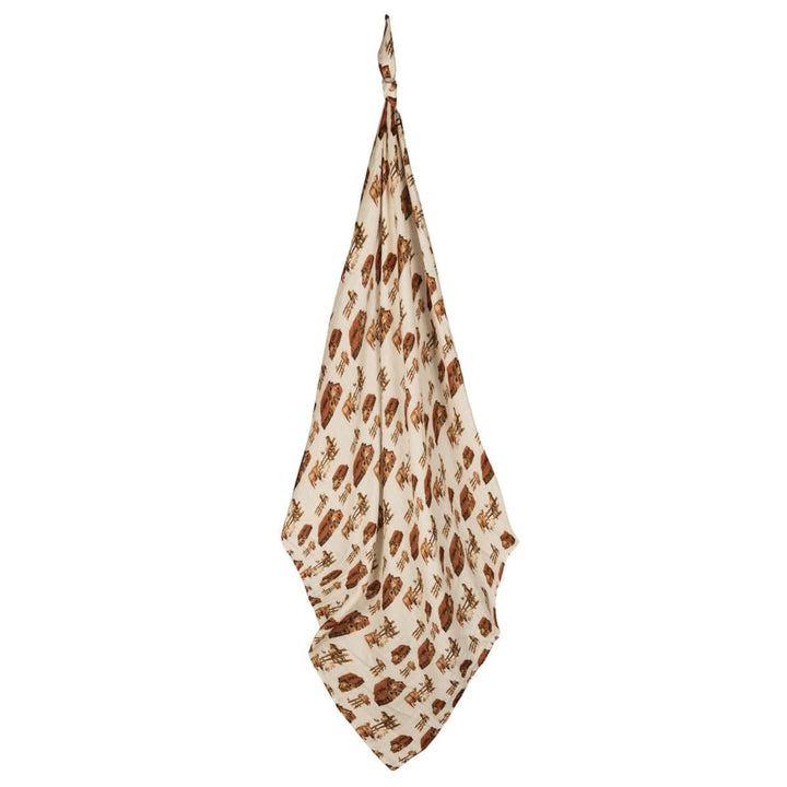 A beige and brown organic cotton Muslin Swaddle Blanket with a leaf print, hanging by one corner.