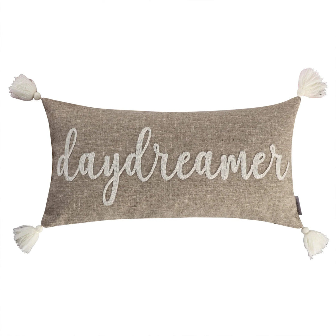 Decorative pillow with 'daydreamer' text and pom-pom ends on a white background