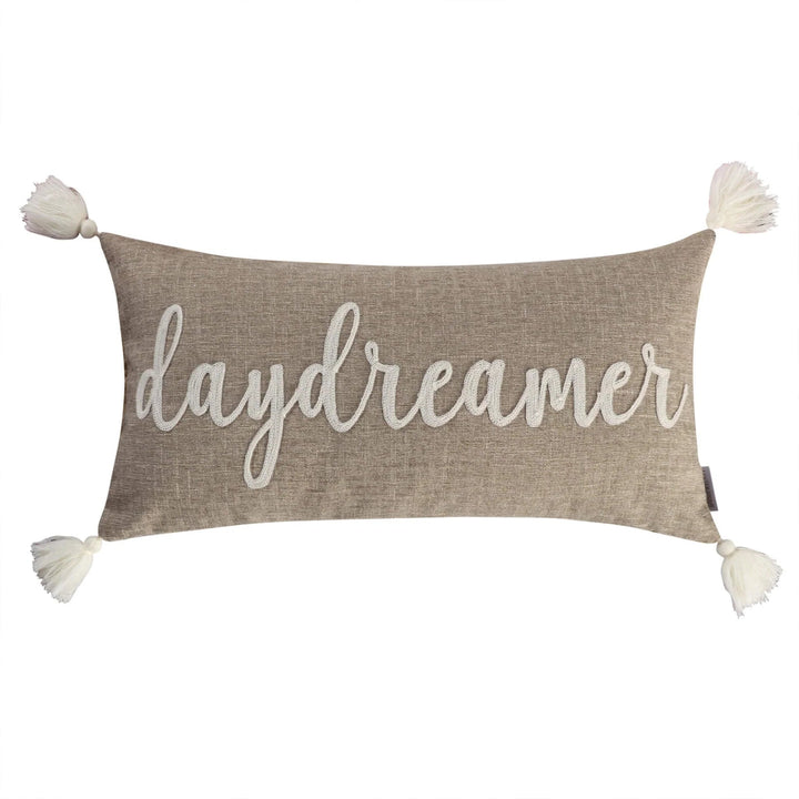 Decorative pillow with 'daydreamer' text and pom-pom ends on a white background