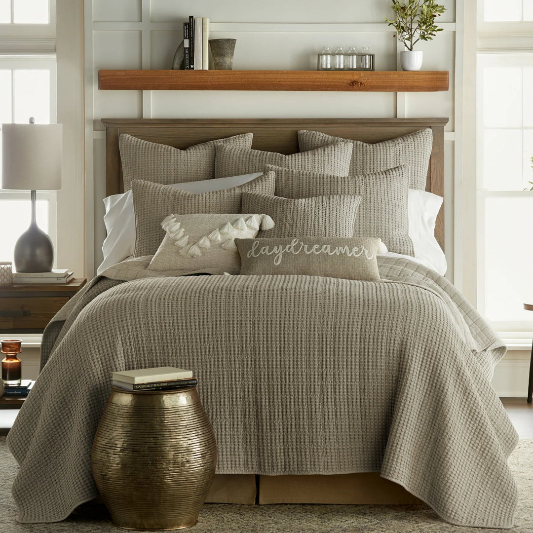 Neatly made bed with gray bedding and pillows in a bedroom setting.