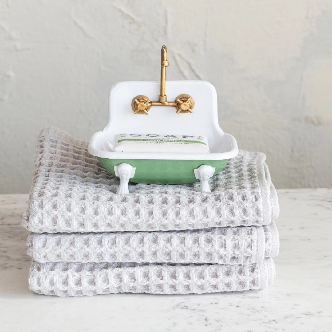 Small decorative sink with a gold faucet on top of folded towels against a neutral background