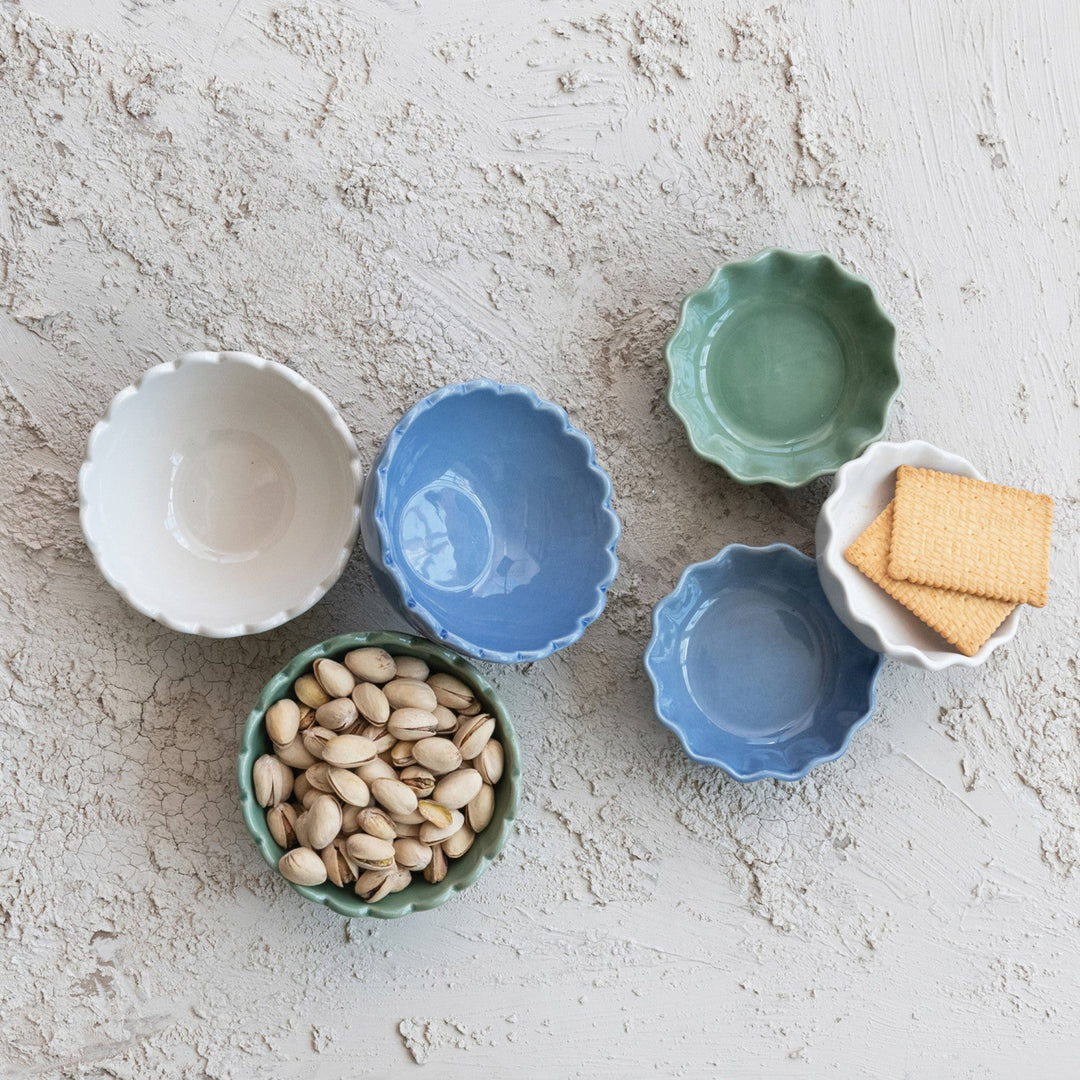 Set of small ceramic bowls in various colors with different contents on a textured surface.
