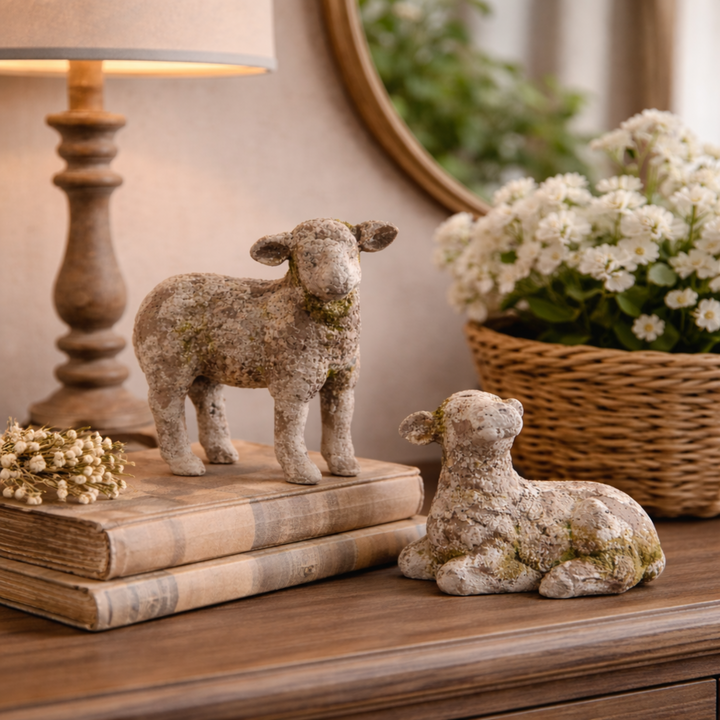Decorative sheep figurines on books with a lamp and flowers in the background
