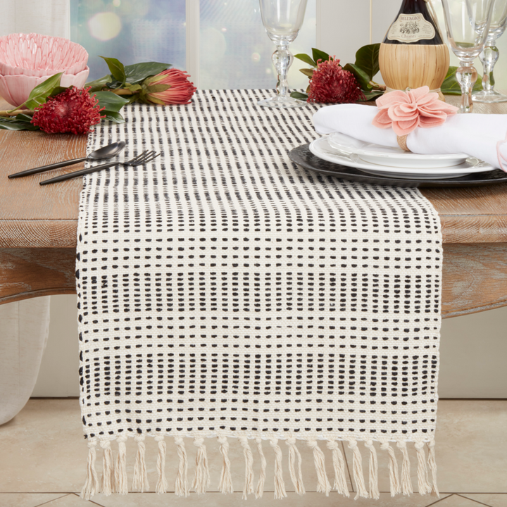 Table setting with a woven table runner, plates, cutlery, and flowers on a wooden table.