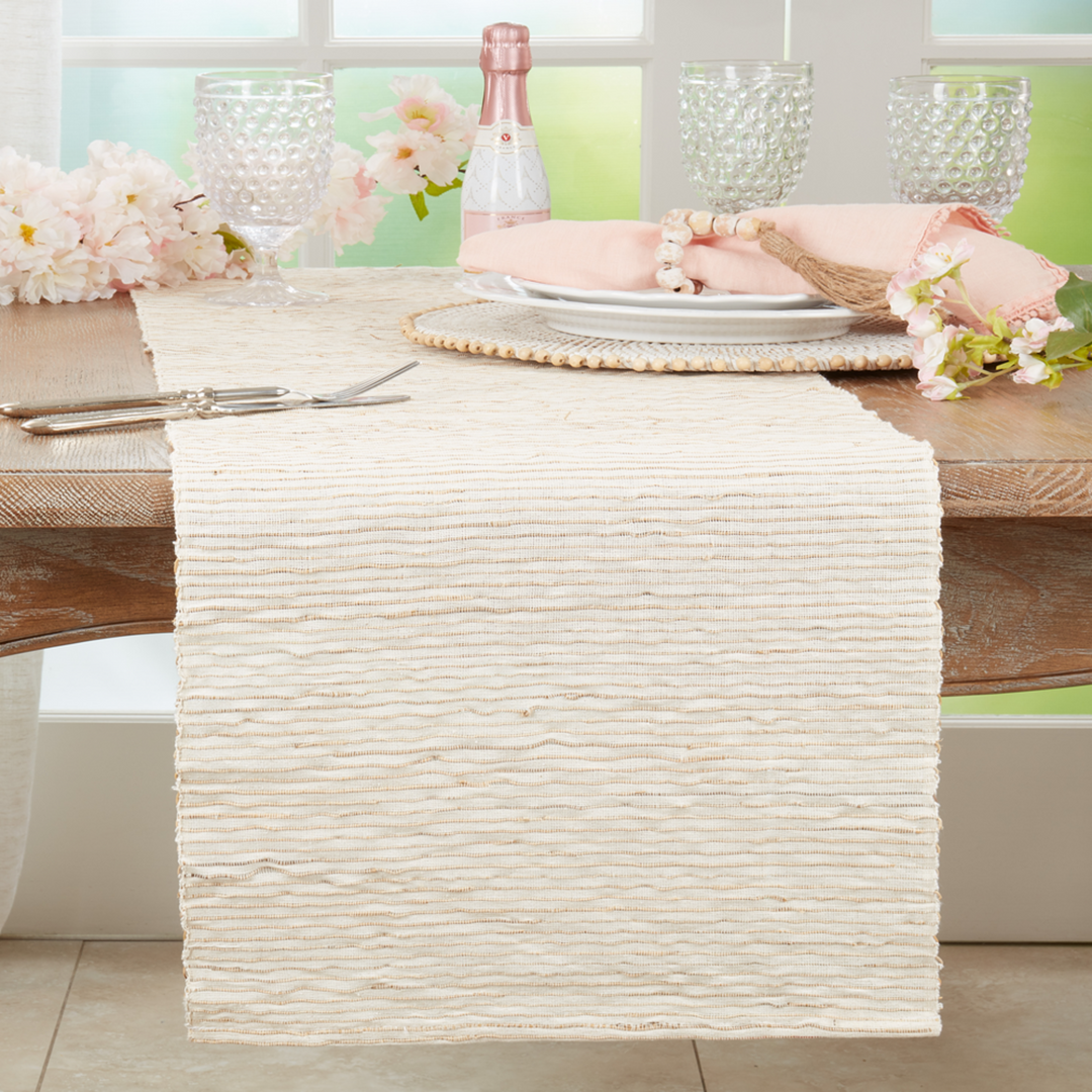 Decorative table setting with a textured white runner, plates, cutlery, and floral arrangements on a wooden table.