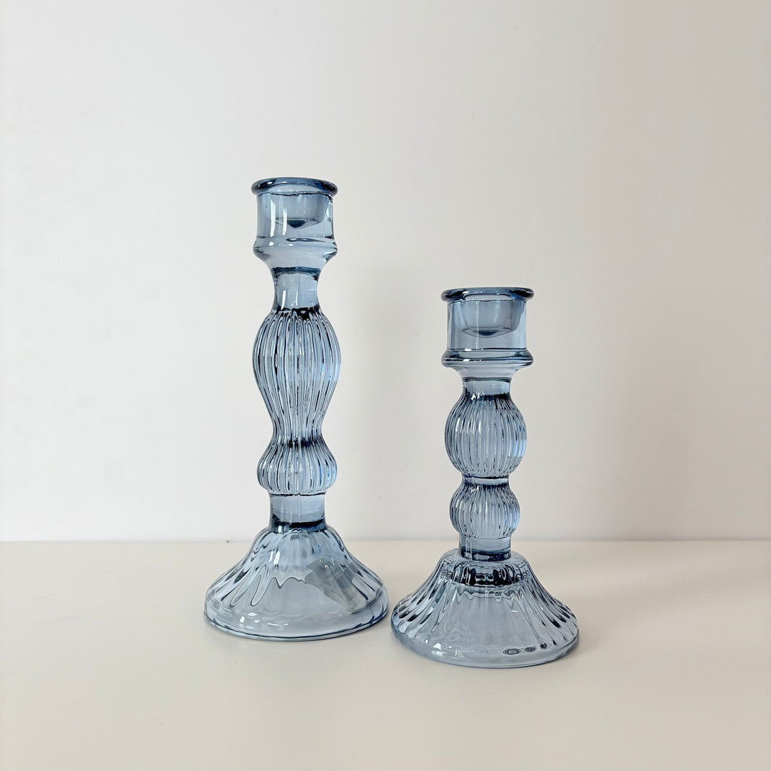 Two blue glass candle holders on a white surface with a light gray background