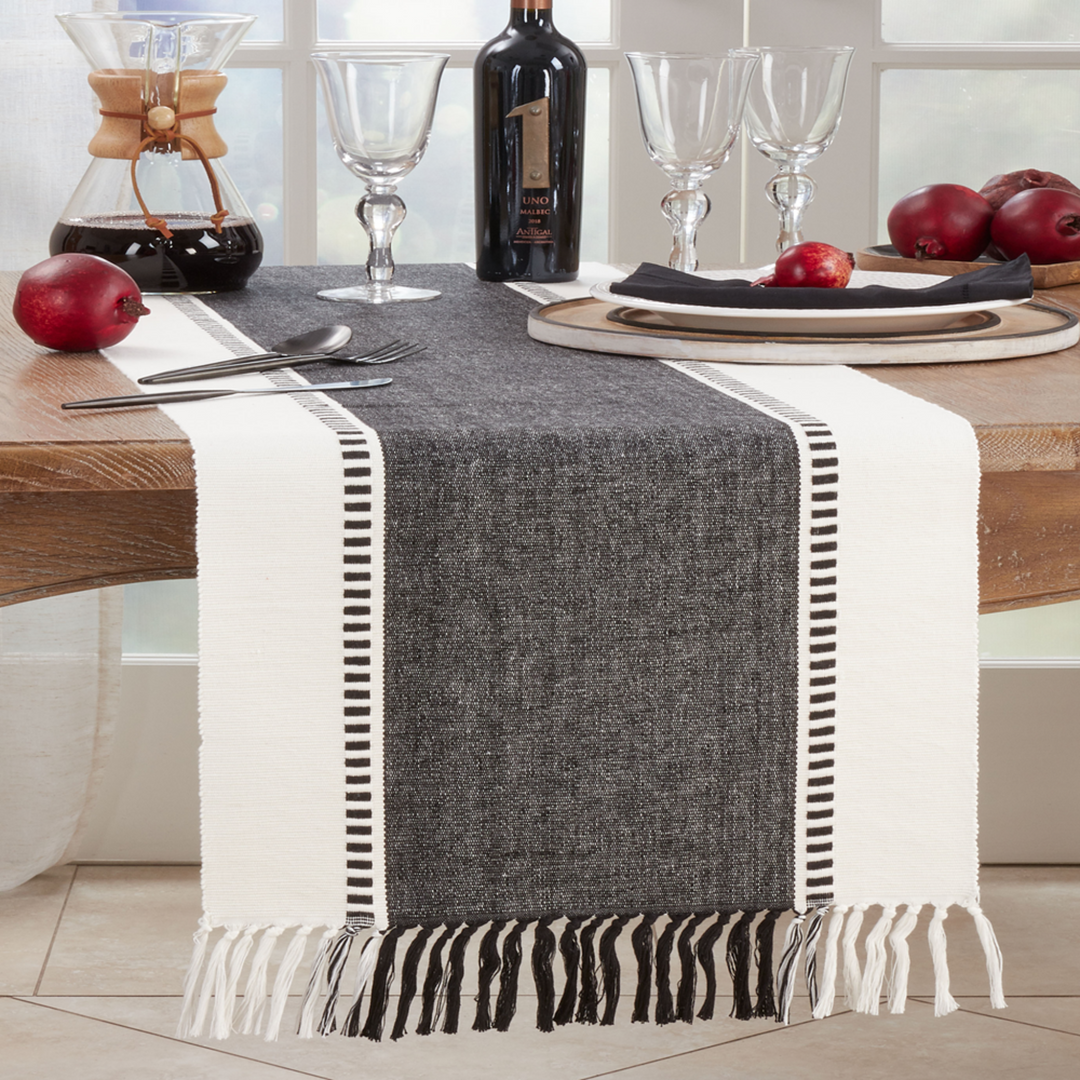 Table setting with a gray and white striped table runner, wine bottle, and fruit on a wooden table.