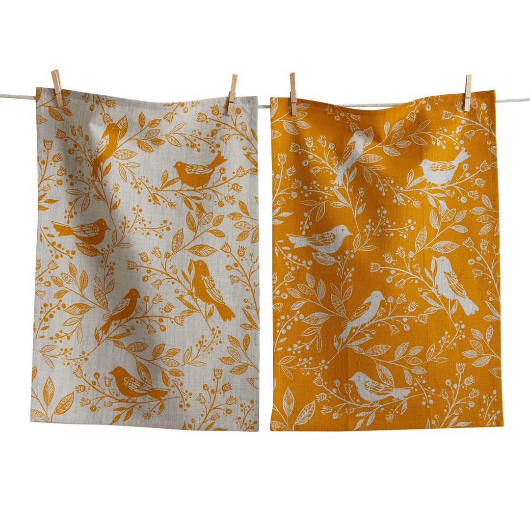 Two fabric towels with bird and floral patterns hanging on a line.