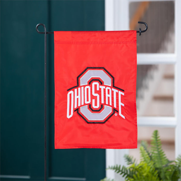 Red Ohio State garden flag hanging on a pole with a blurred background