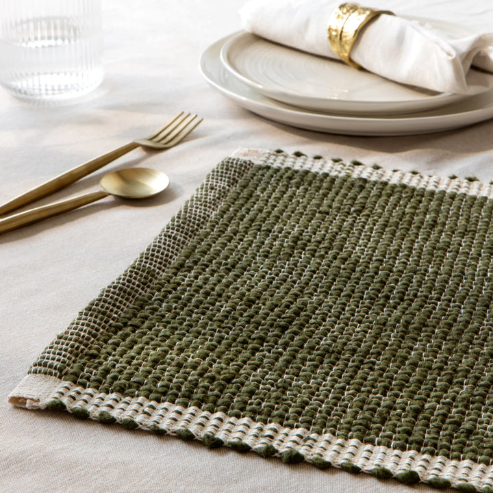 Green woven placemat on a table with white plates and gold cutlery.