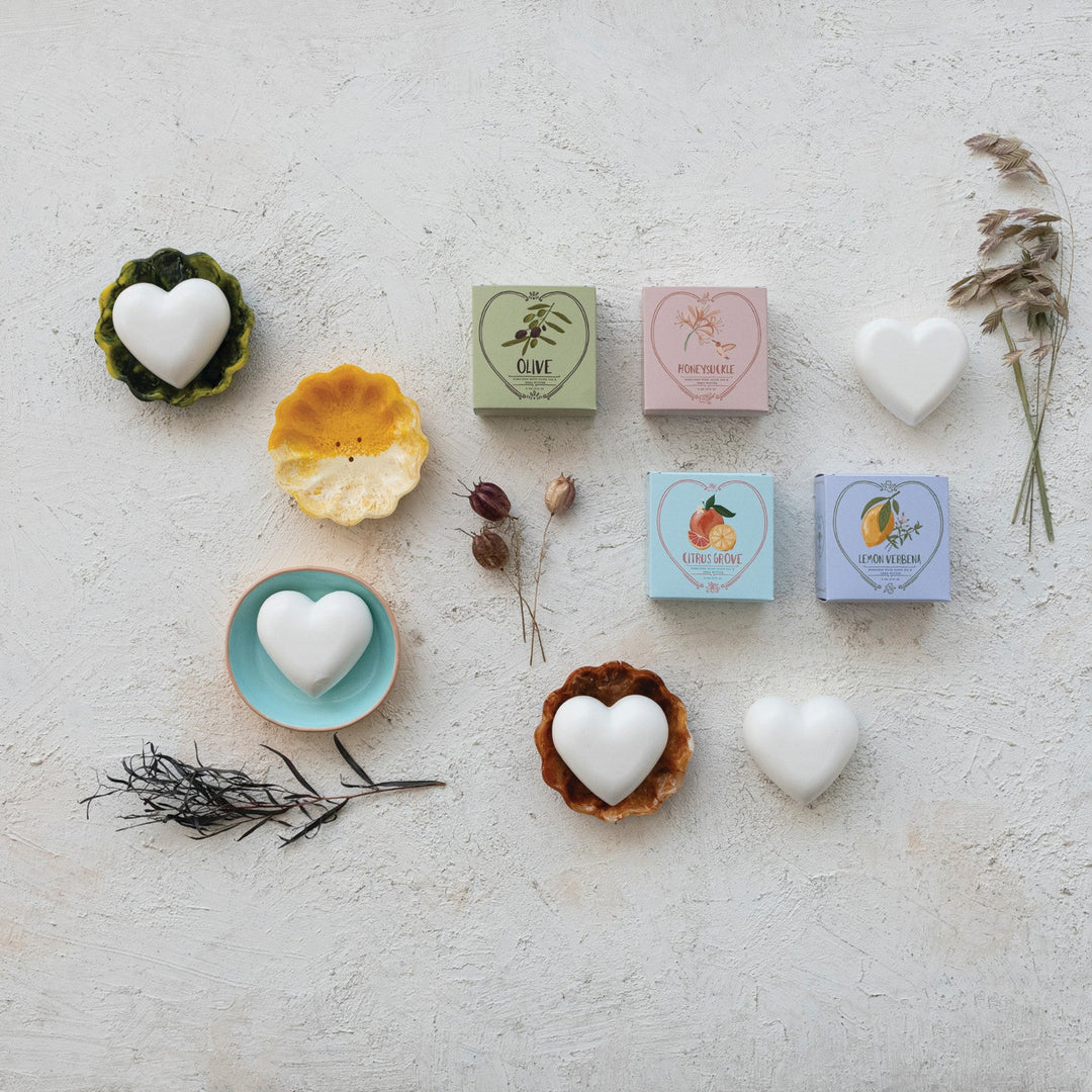 Heart-shaped soap bars and boxes on a textured surface with dried plants.