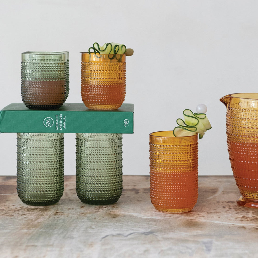 Set of colorful glassware including cups and a pitcher on a wooden surface with a white background.