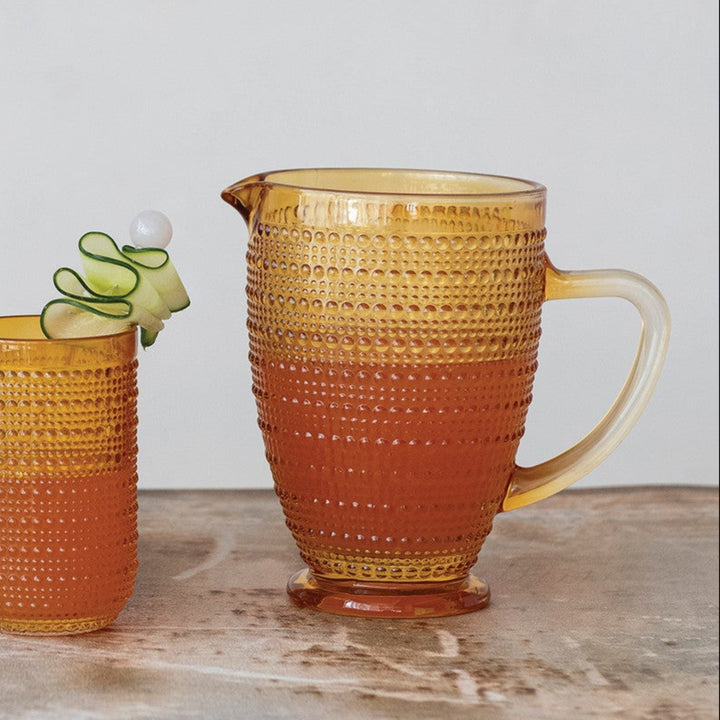 Set of colorful glassware including cups and a pitcher on a wooden surface with a white background.