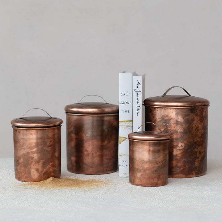 Set of four copper canisters on a light surface with a neutral background