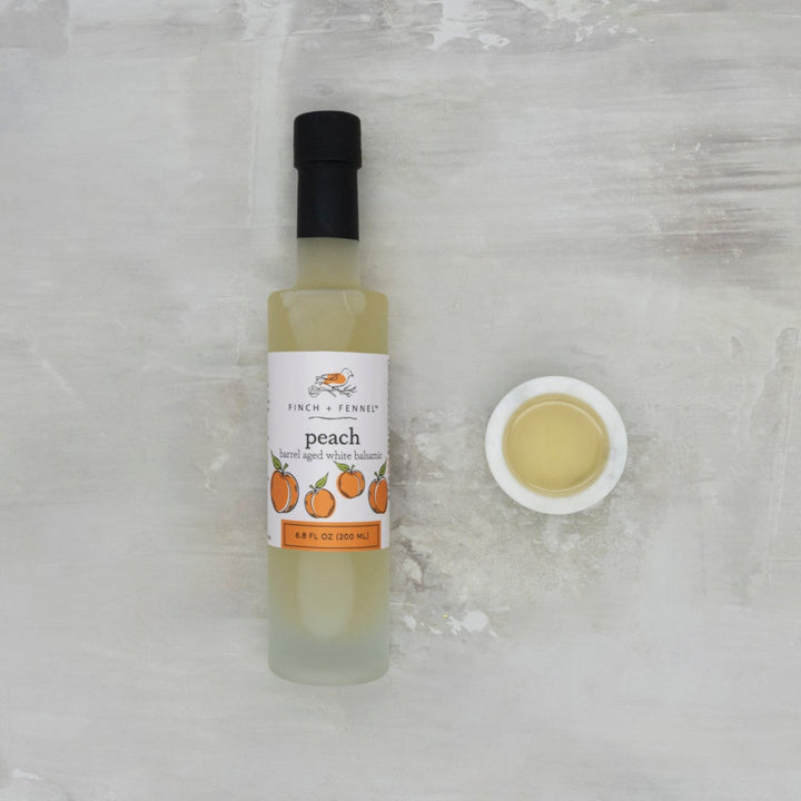 Bottle of peach-flavored oil with a small dish of oil on a textured white background