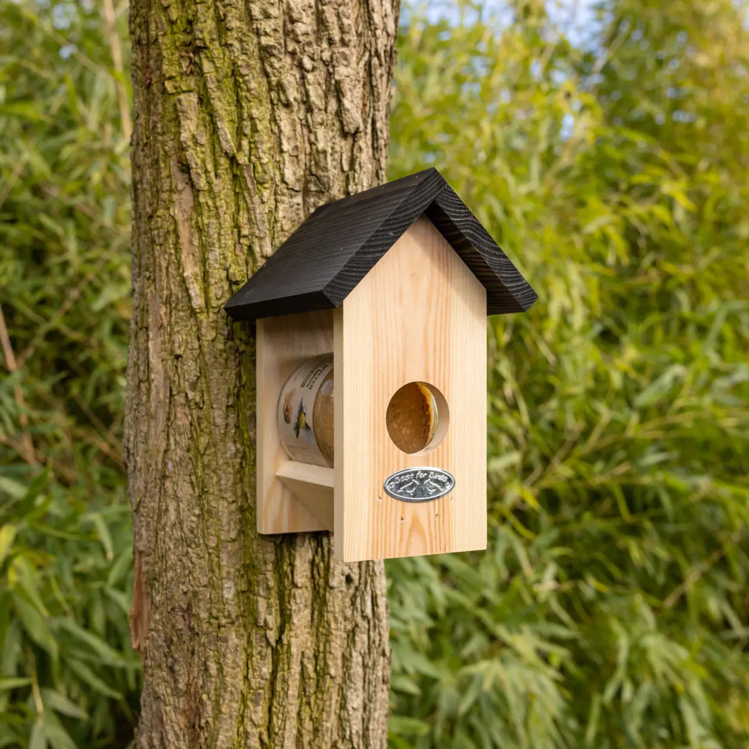 Wooden birdhouse attached to a tree trunk with green foliage in the background
