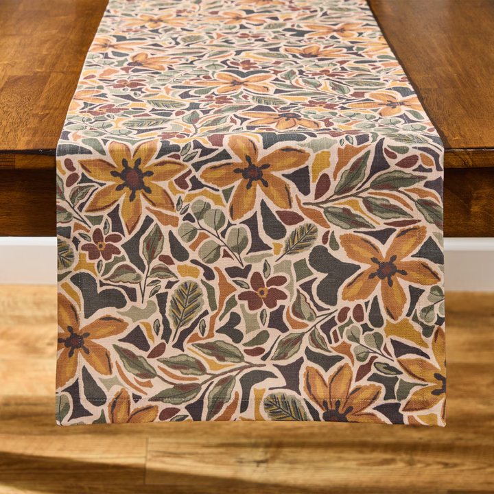 A floral table runner with a vintage botanical pattern in orange, brown, beige, and gray, draped over a wooden table.