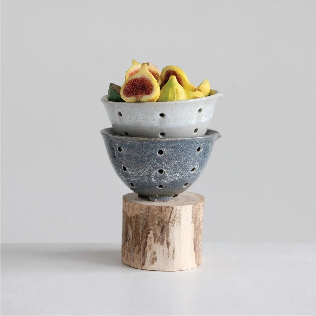 Stacked ceramic bowls with fruits on a wooden block against a light gray background