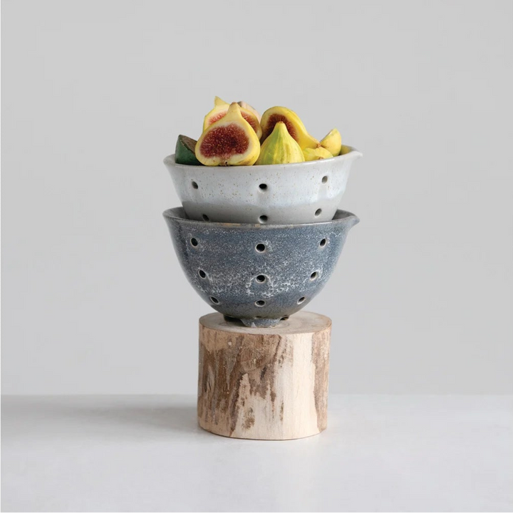 Stacked ceramic bowls with fruits on a wooden block against a light gray background