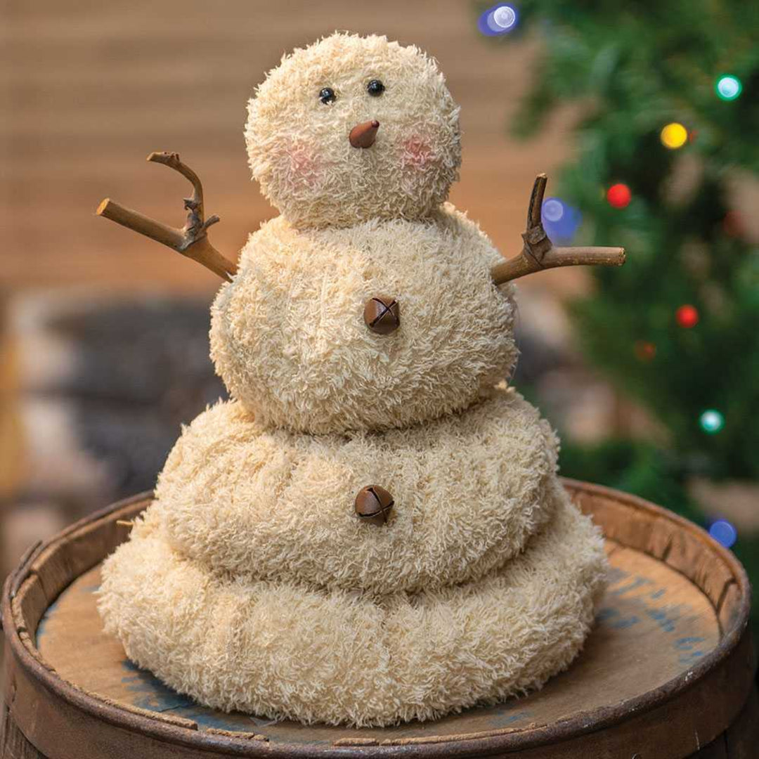 Decorative snowman figure on a wooden surface with a blurred Christmas tree in the background.