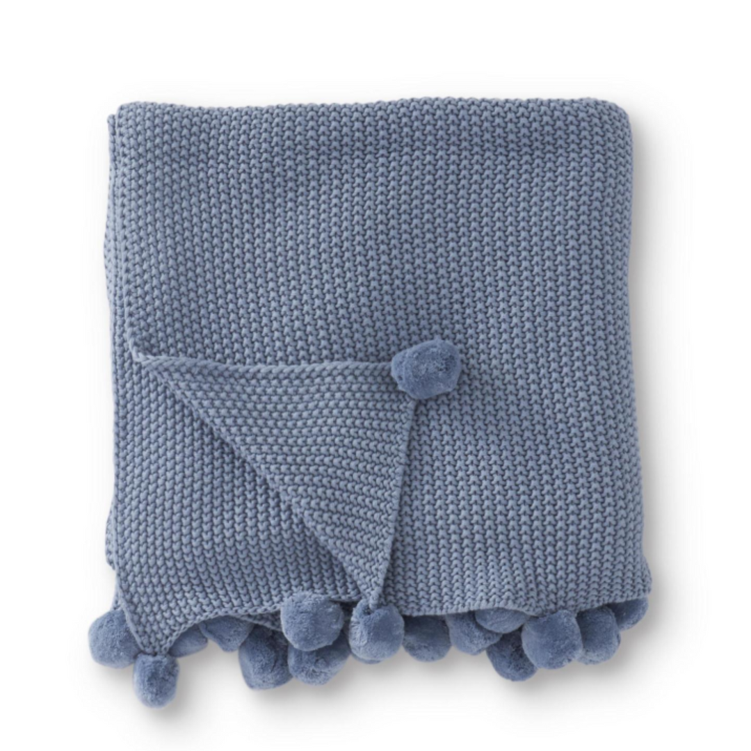 Blue knitted blanket with pom-pom trim on a white background