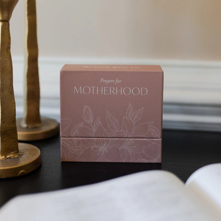 Pink box titled 'Prayers for Motherhood' on a dark surface with a blurred background