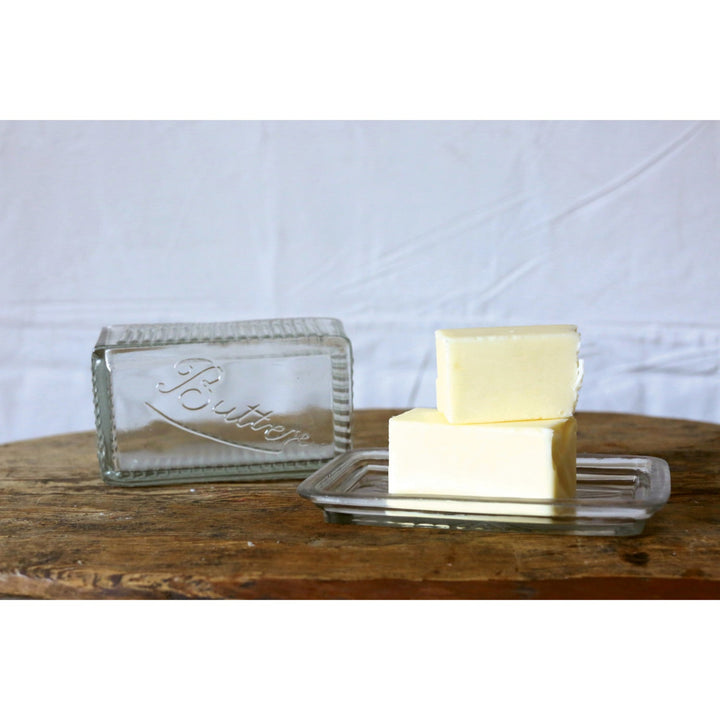 Two blocks of butter on a glass 'To Butter' dish with a white background