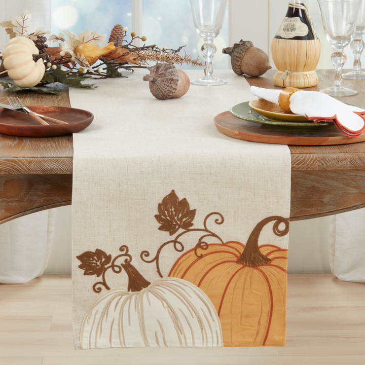 Table setting with a decorative table runner featuring pumpkins and leaves on a wooden table.