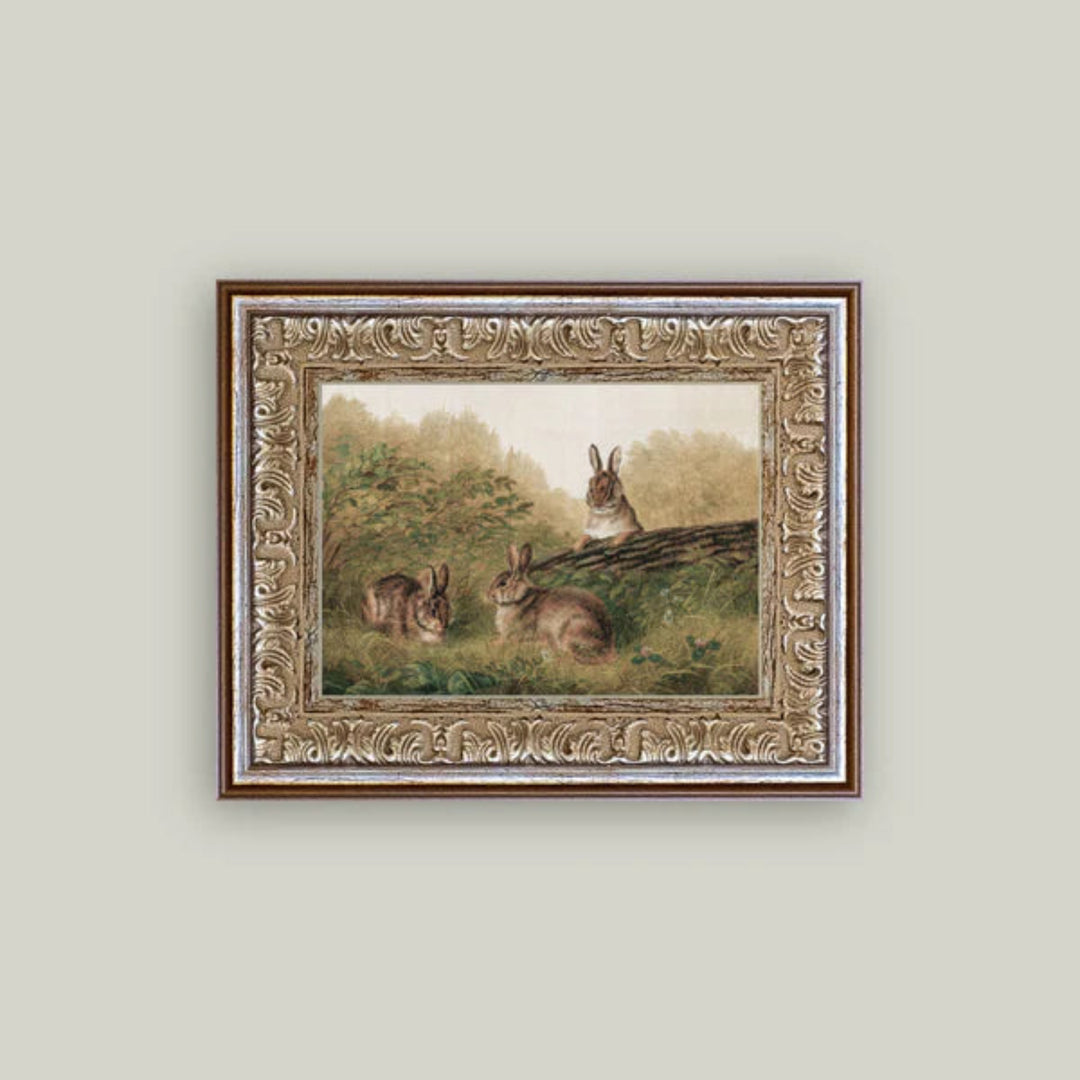 Framed painting of rabbits on a grassy hill with a decorative frame.