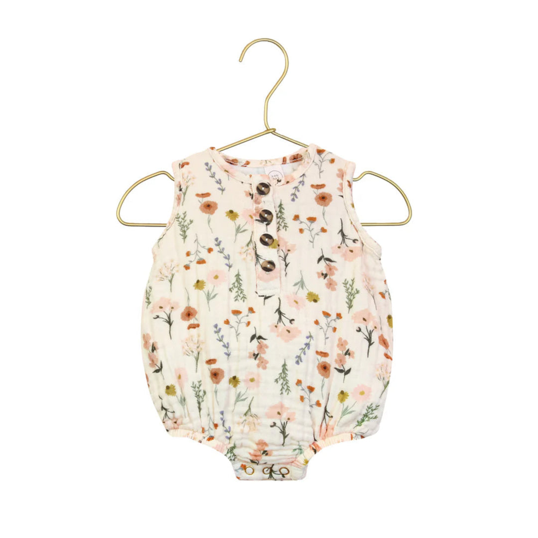 A sleeveless baby romper with a soft floral print, hanging on a gold metal hanger against a plain white background.