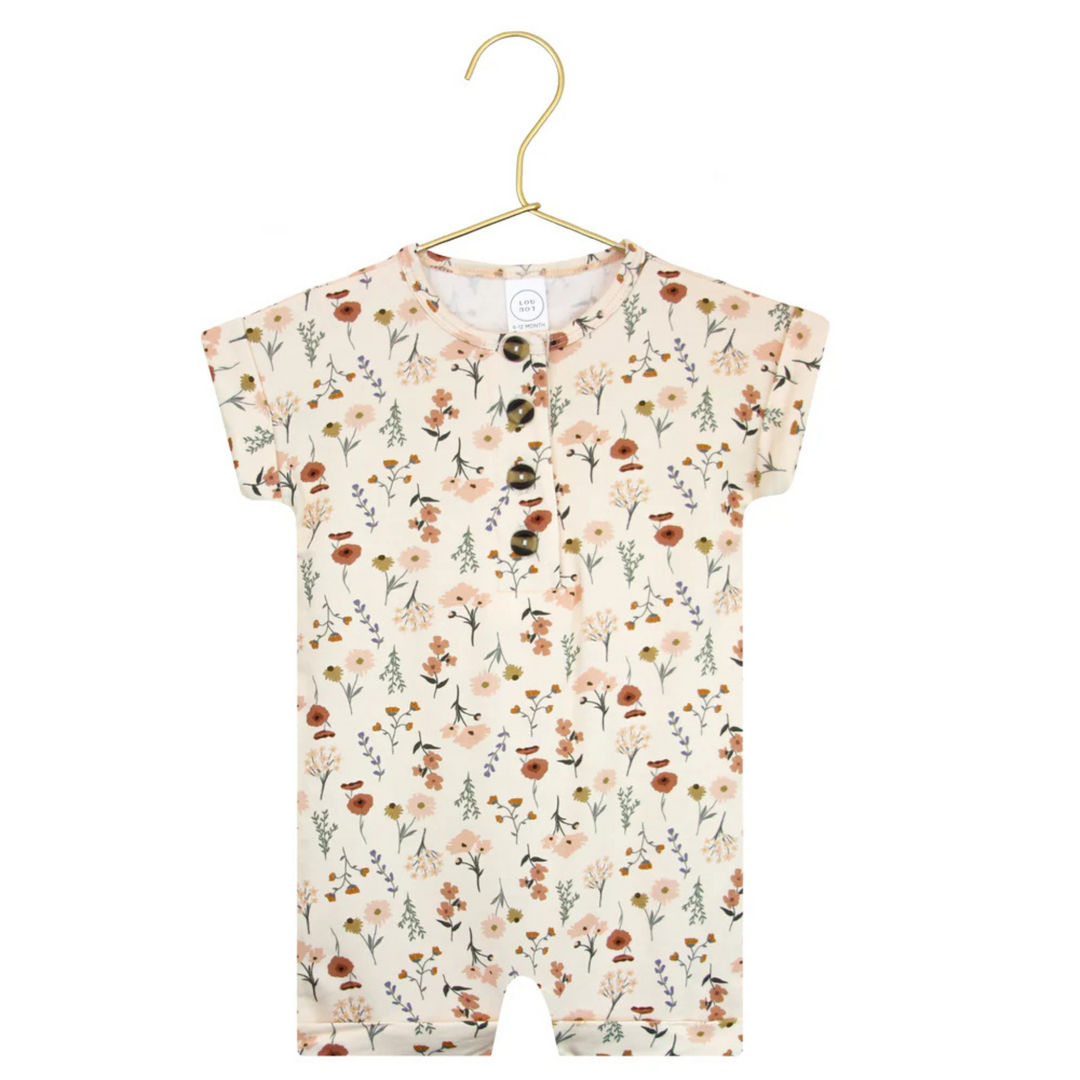 A baby short-sleeve romper with a floral print, hanging on a gold hanger against a white background, with a circular inset showing a close-up of the fabric pattern.