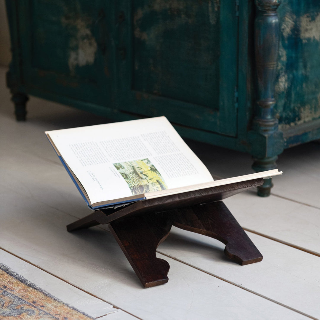 Open book on a wooden stand with a vintage cabinet in the background
