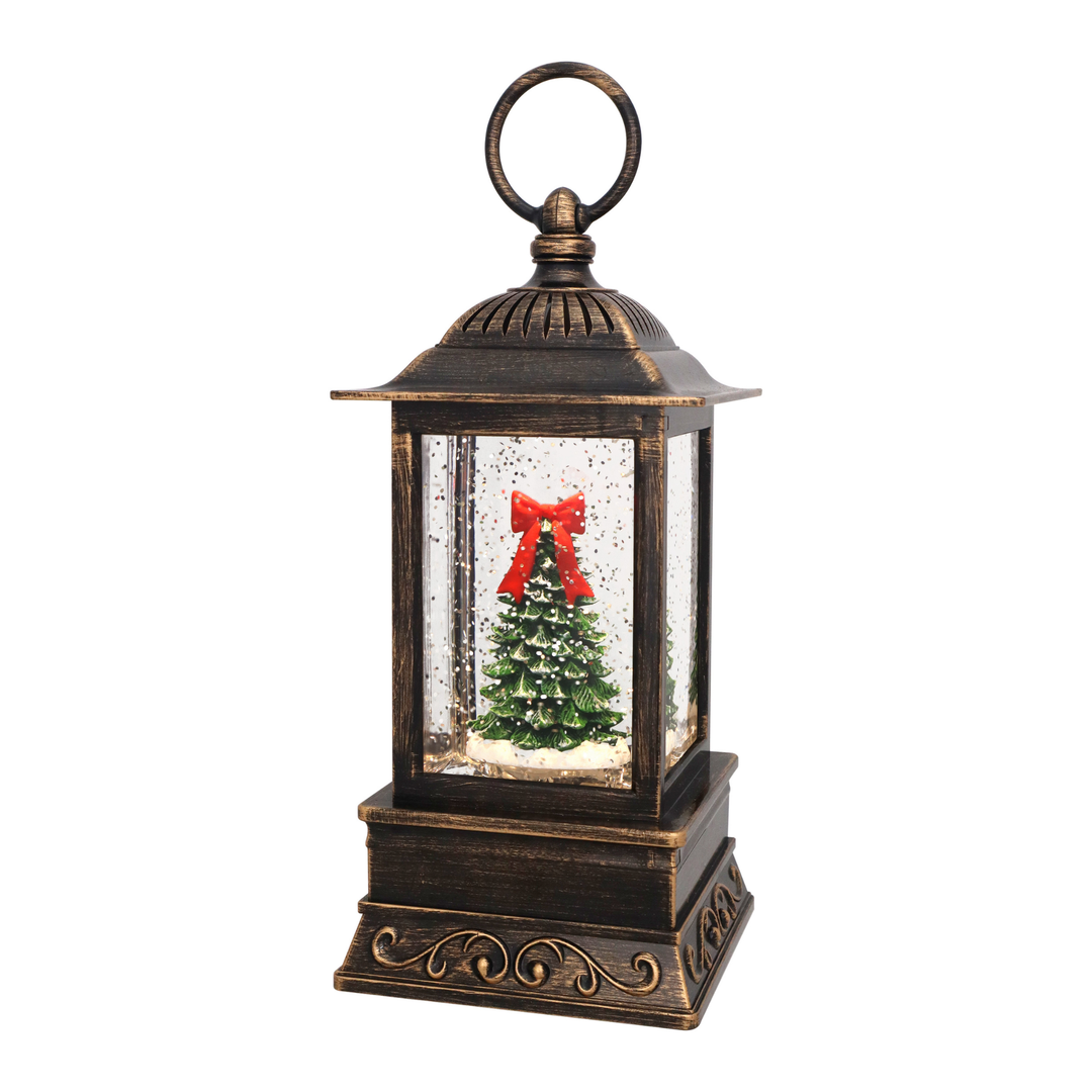 A decorative lantern-style Christmas tree snow globe with an antique bronze finish, featuring a miniature green Christmas tree with a red bow inside clear glass panels on a white background.