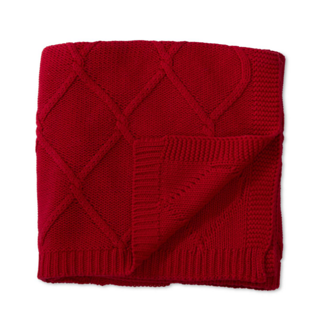 A folded red knit throw blanket with a diamond cable pattern and ribbed border, shown on a plain white background.