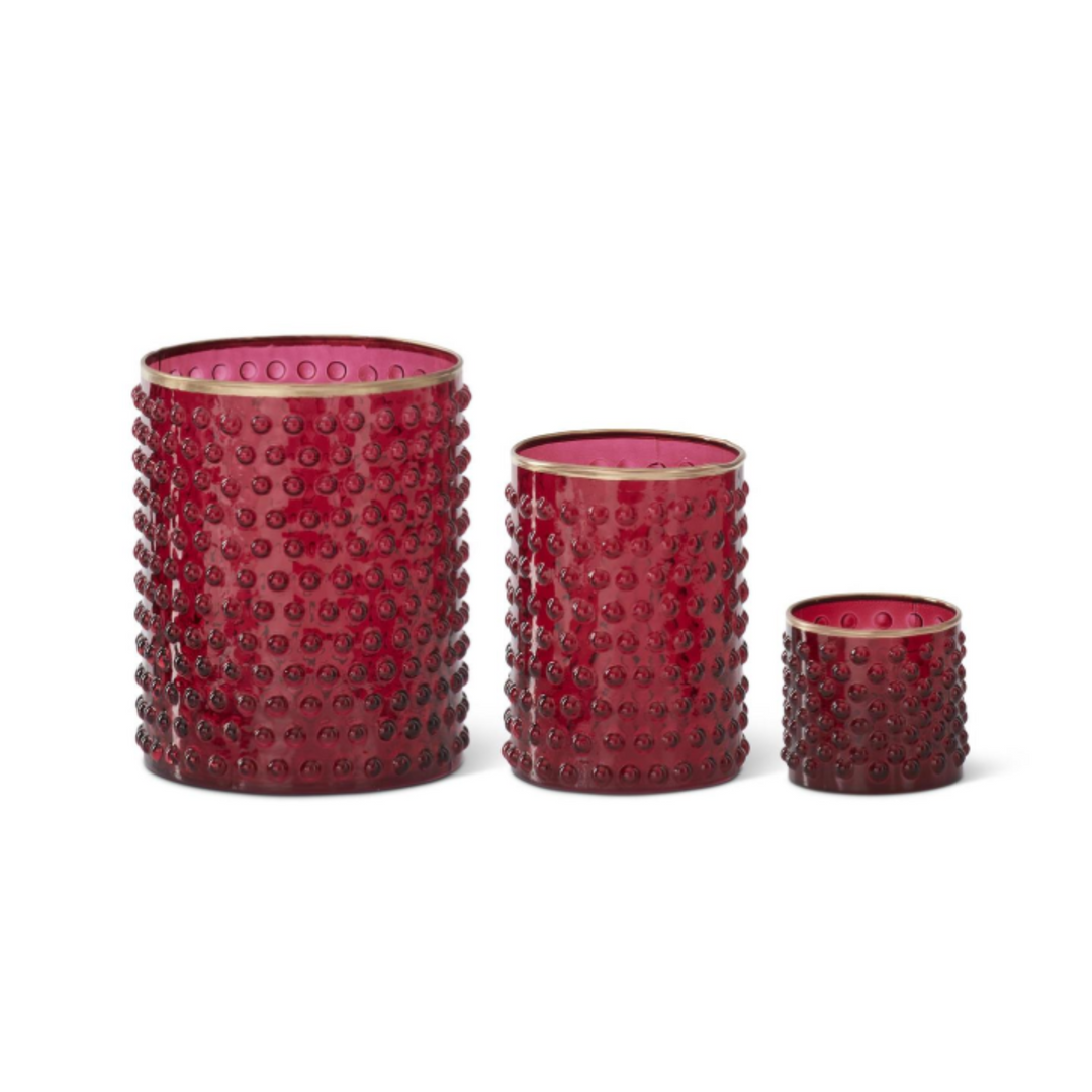 Three red textured glass candle holders of different sizes with gold rims, arranged from largest to smallest on a white background.