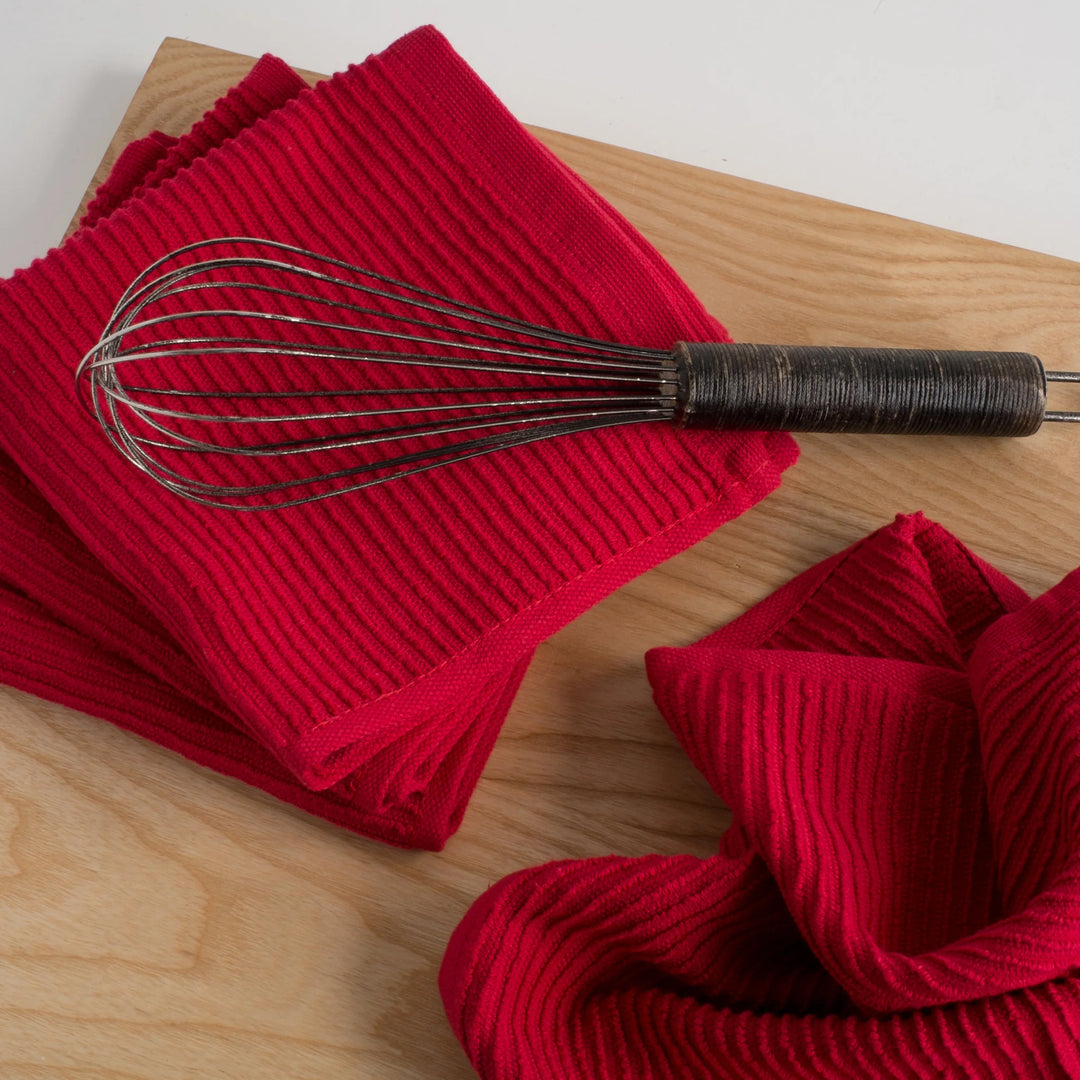 Red ribbed kitchen towels with a metal whisk on a wooden surface